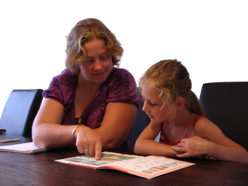 Je ziet hier Annemieke Augusteijn en een leerling die samen aan tafel zitten. Op de tafel ligt een opengeslagen boek. Annemieke wijst in dit boek een afbeelding aan, de leerling kijkt hiernaar.